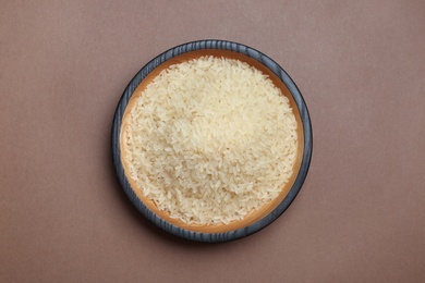 Photo of Parboiled rice in wooden bowl on color background, top view