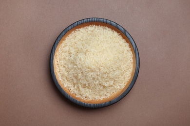 Parboiled rice in wooden bowl on color background, top view