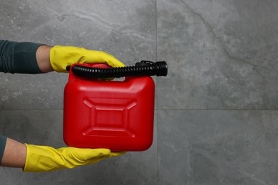 Photo of Man in rubber gloves holding red canister near grey wall, closeup. Space for text