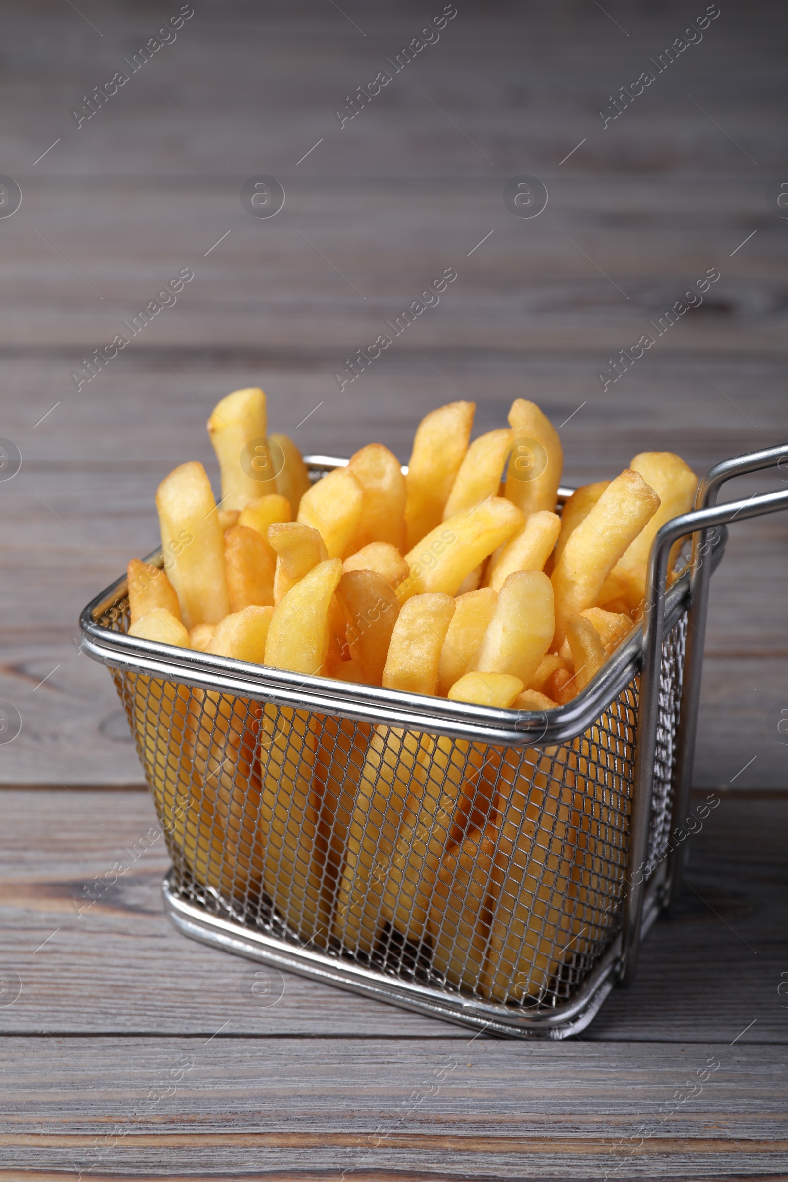 Photo of Metal basket with tasty French fries on grey wooden table