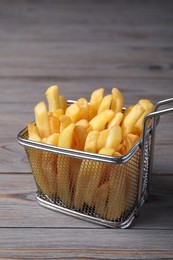 Metal basket with tasty French fries on grey wooden table