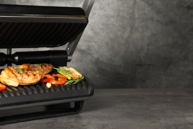 Electric grill with tasty meat, spices and vegetables on grey textured table, space for text