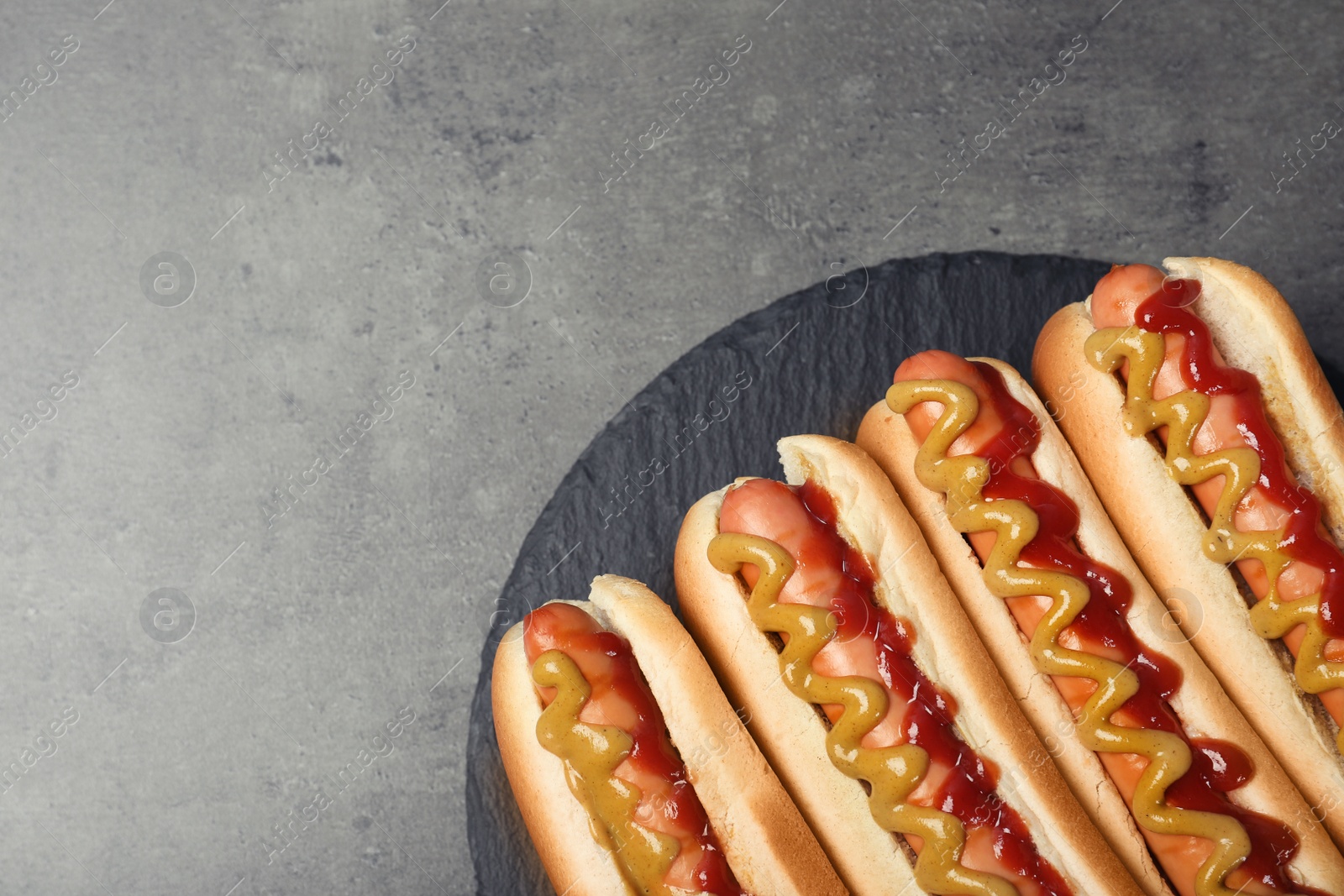 Photo of Slate plate with hot dogs on grey background, top view. Space for text
