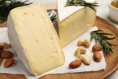 Plate with pieces of tasty camembert cheese, nuts and rosemary on table, closeup