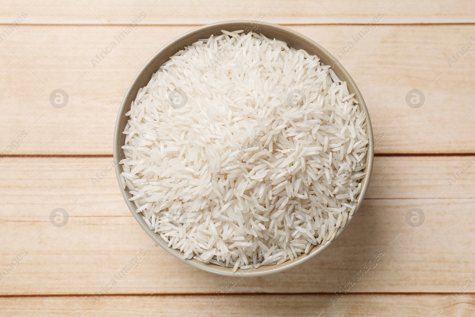 Photo of Raw basmati rice in bowl on white wooden table, top view