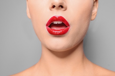 Photo of Beautiful young woman with red glossy lips on gray background, closeup