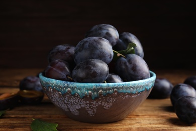 Delicious ripe plums in bowl on wooden table