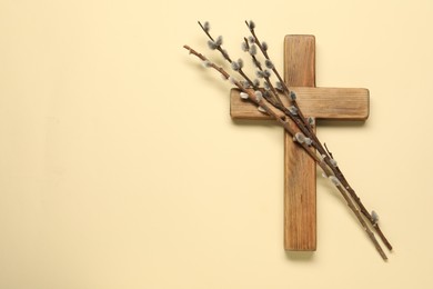 Photo of Wooden cross and willow branches on beige background, top view with space for text. Easter attributes