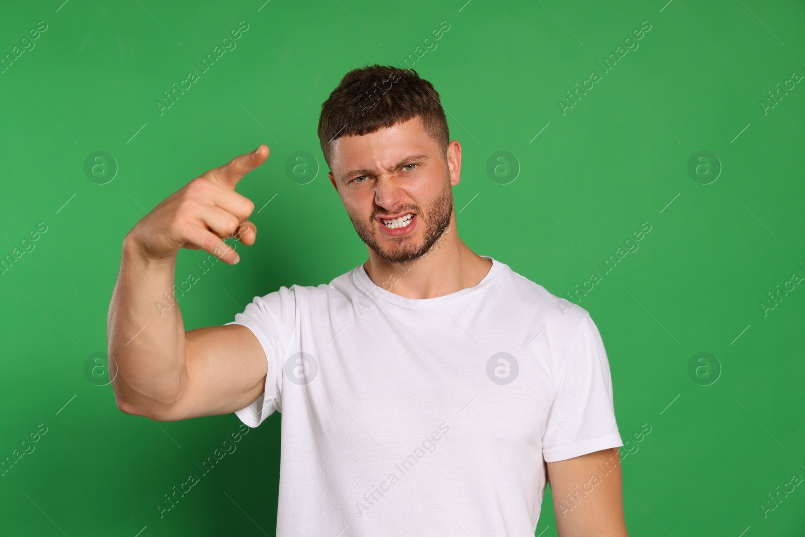 Photo of Aggressive young man pointing on green background