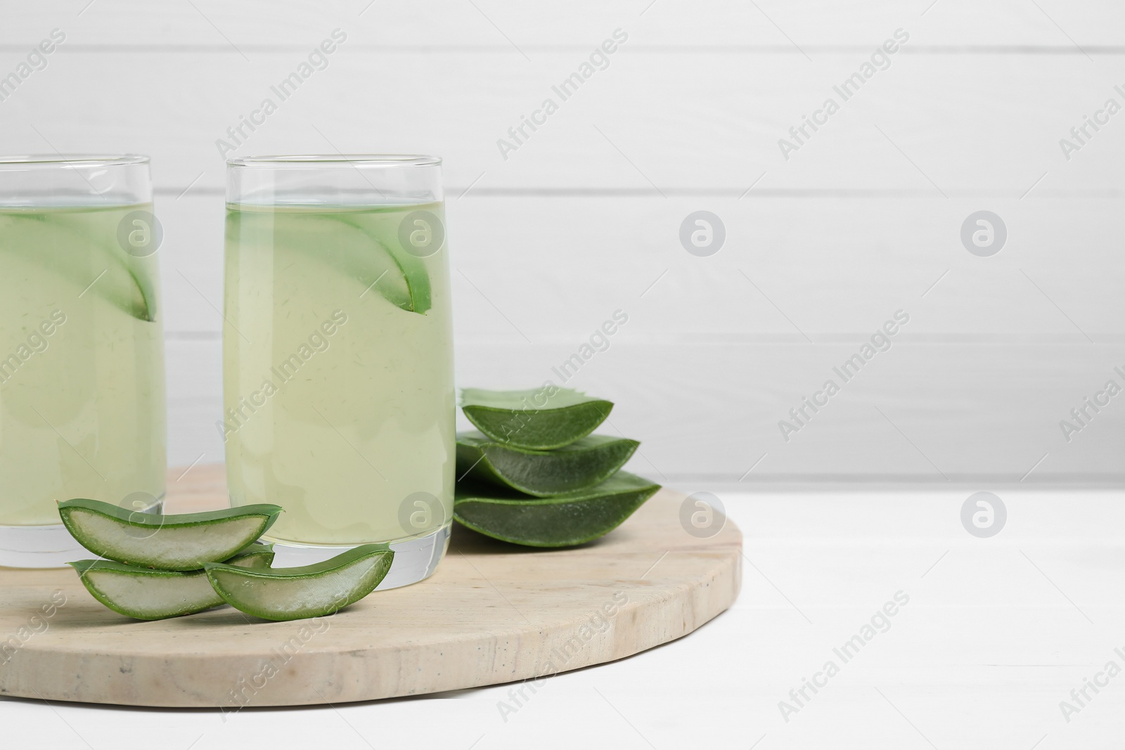 Photo of Tasty aloe juice in glasses and cut fresh leaves on white table, space for text