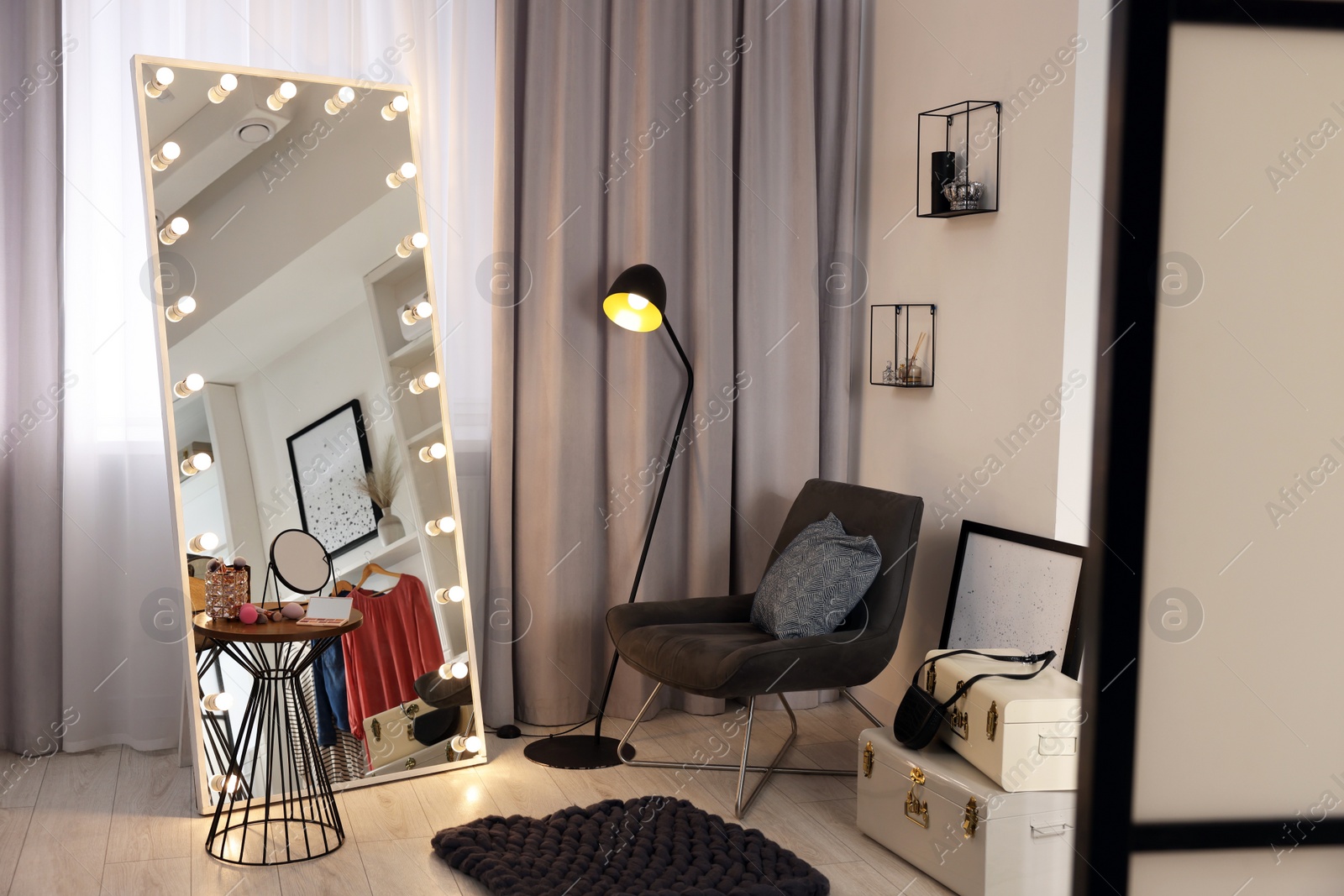 Photo of Makeup room. Stylish mirror with light bulbs, beauty products on table and armchair indoors