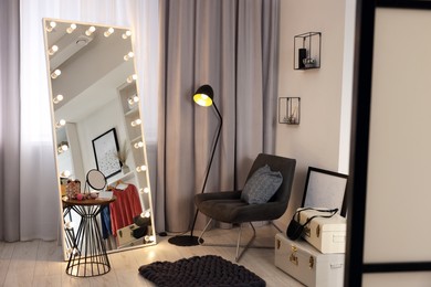 Photo of Makeup room. Stylish mirror with light bulbs, beauty products on table and armchair indoors