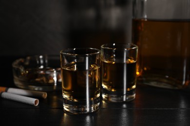Photo of Alcohol addiction. Whiskey in glasses, cigarettes and ashtray on black wooden table