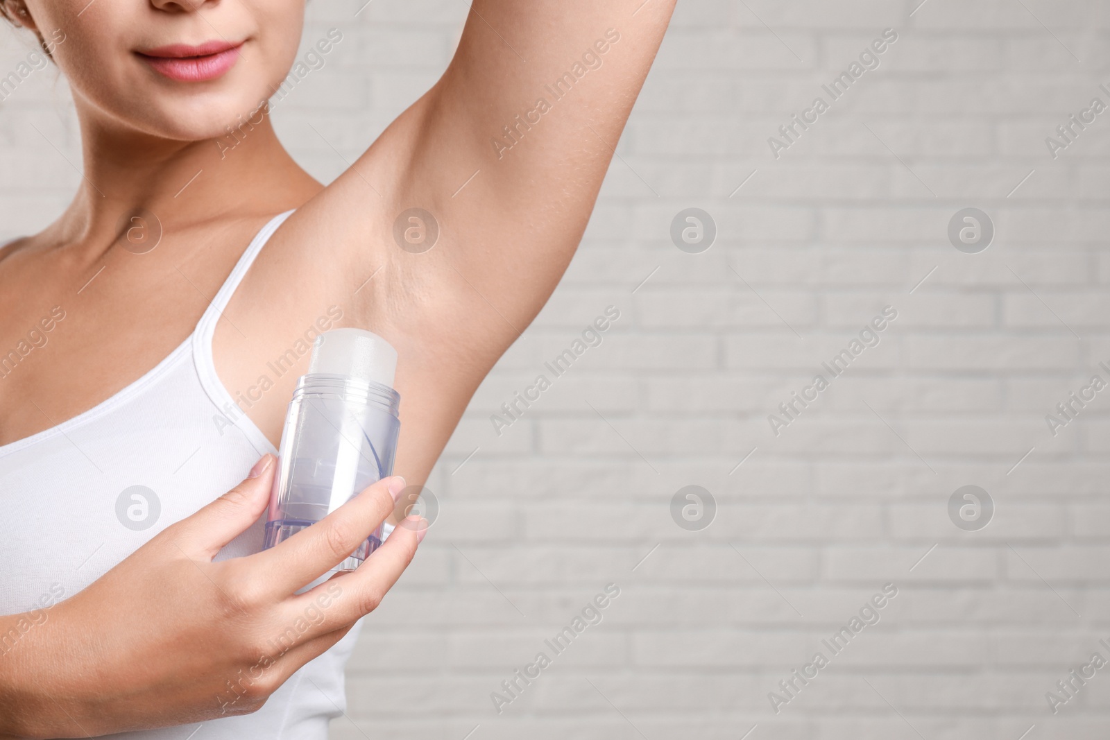 Photo of Young woman applying crystal alum deodorant to armpit against brick wall, closeup. Space for text