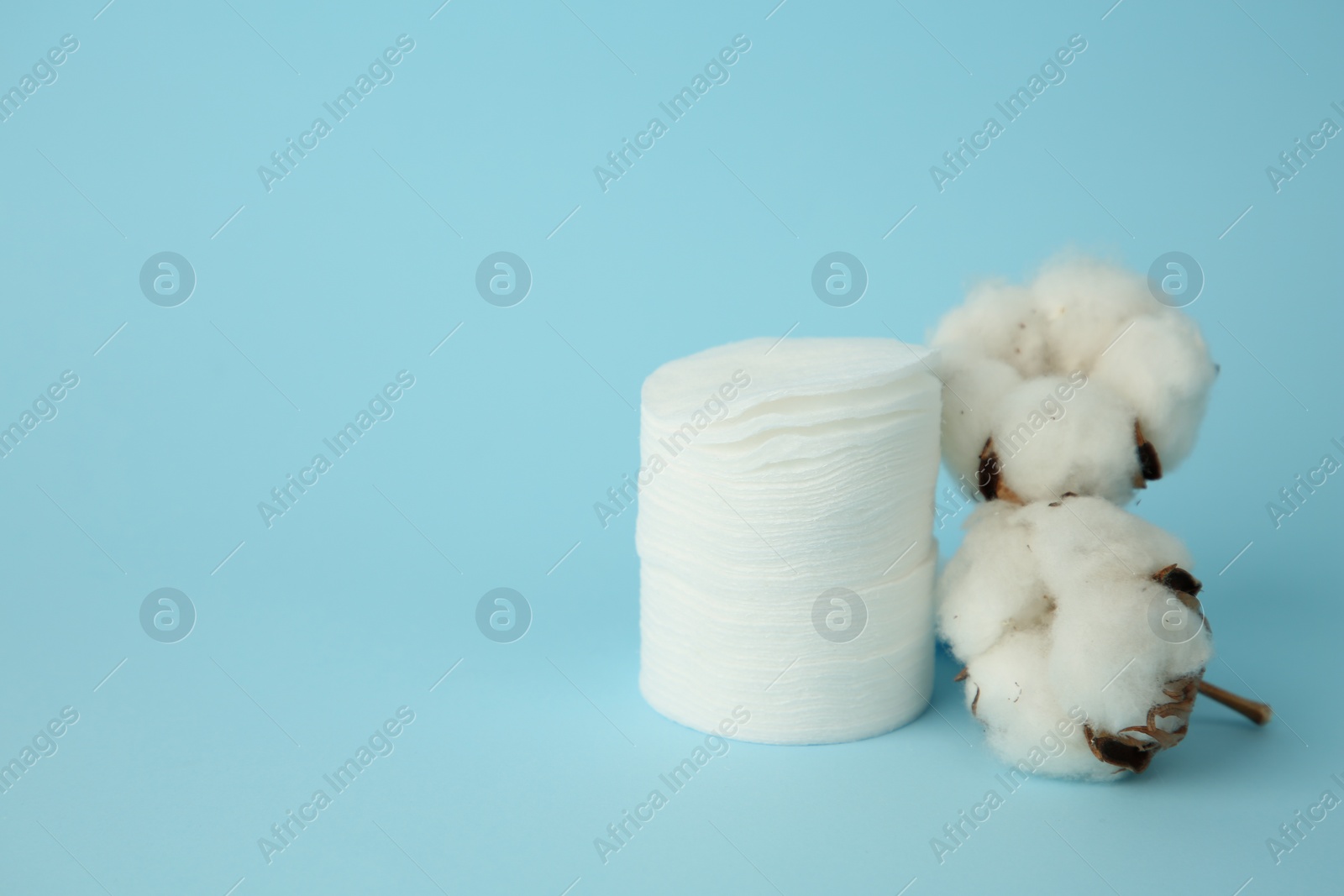 Photo of Stack of cotton pads and flowers on light blue background. Space for text