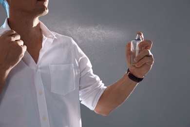 Photo of Young man spraying perfume on gray background