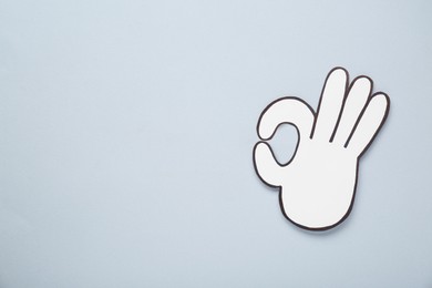 Paper cutout of okay hand gesture on light grey background, top view. Space for text