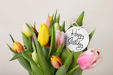 Image of Beautiful bouquet of tulip flowers with Happy Birthday card on light background, closeup