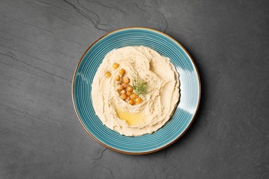 Photo of Plate of tasty hummus with garnish on black table, top view