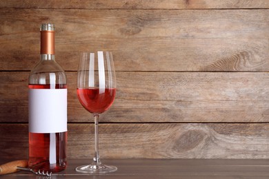 Corkscrew near bottle and glass of delicious rose wine on table against wooden background. Space for text