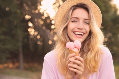 Happy young woman with delicious ice cream in waffle cone outdoors. Space for text