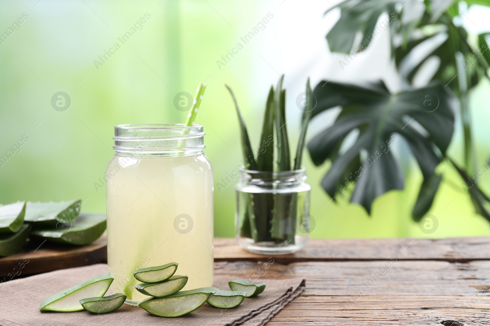 Photo of Fresh aloe juice in jar with straw and leaves on wooden table outdoors. Space for text