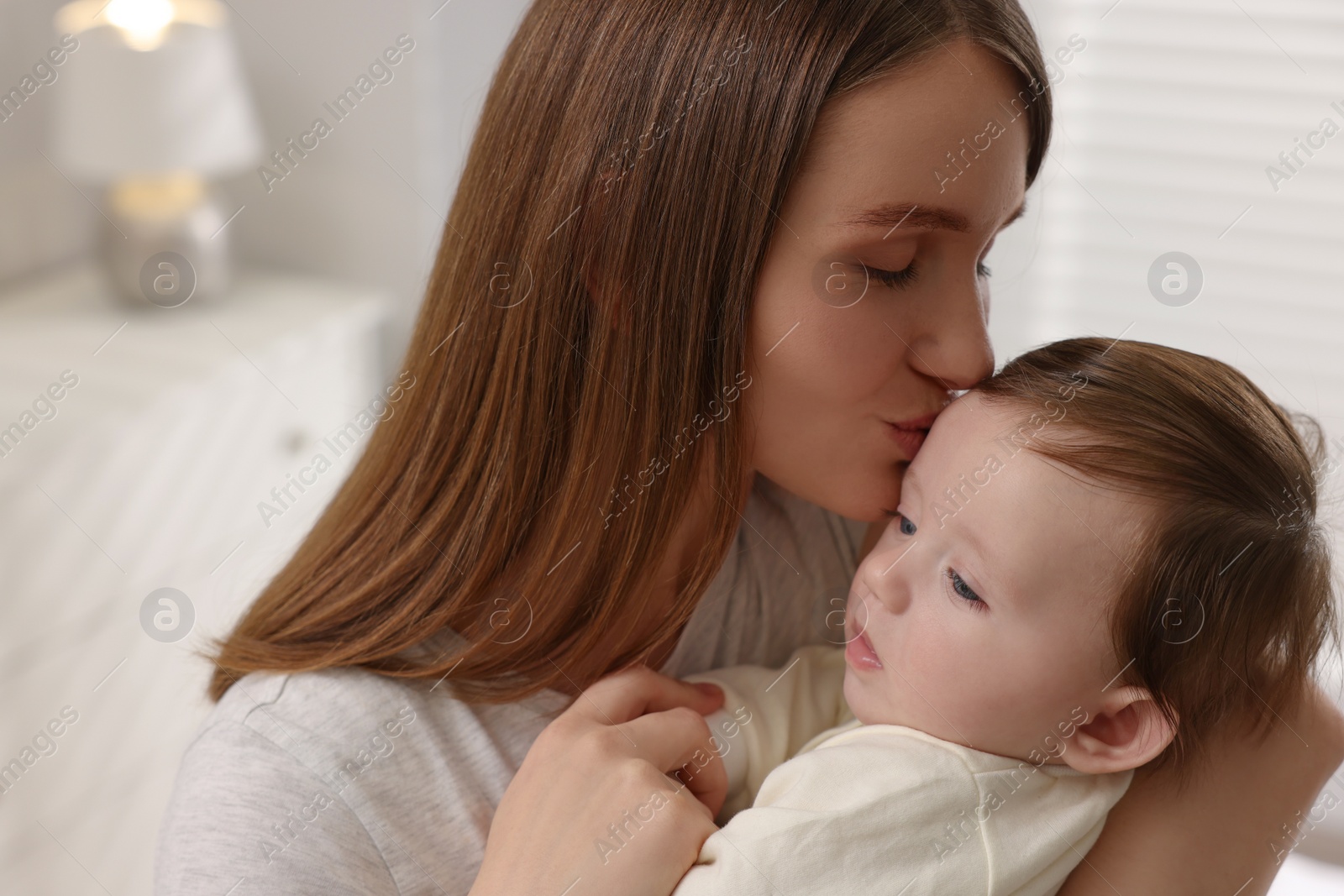 Photo of Happy mother kissing her little baby indoors, closeup