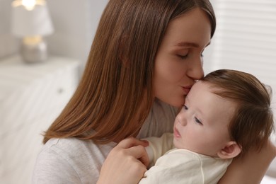 Happy mother kissing her little baby indoors, closeup