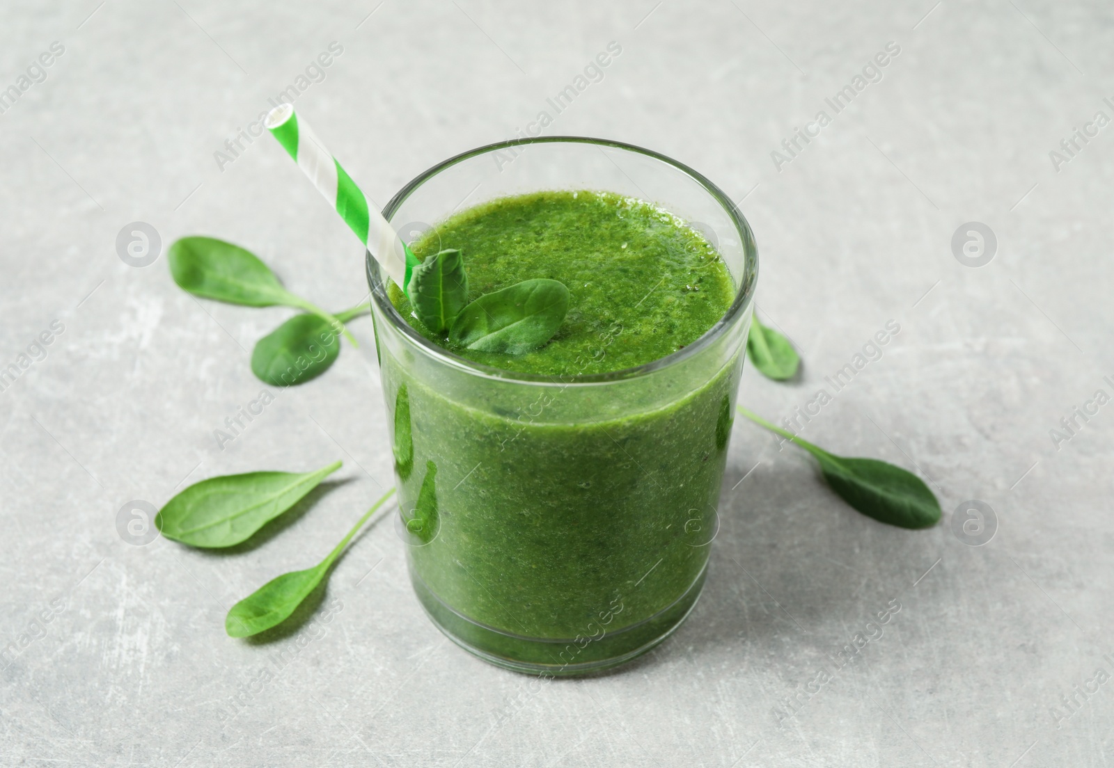 Photo of Green juice and fresh spinach leaves on light grey table