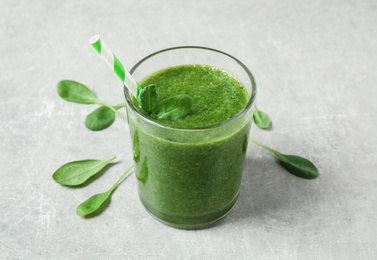 Photo of Green juice and fresh spinach leaves on light grey table