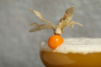 Refreshing cocktail decorated with physalis fruit on grey background, closeup