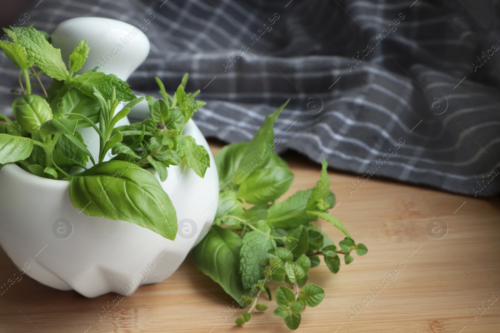 Photo of Mortar with different fresh herbs on wooden table, closeup. Space for text