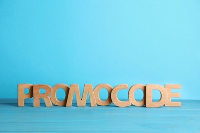 Photo of Words Promo Code made of wooden letters on turquoise table, space for text