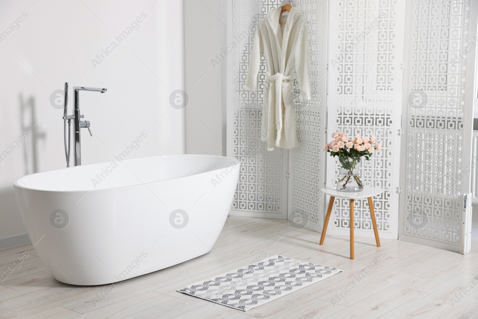 Photo of Stylish bathroom interior with ceramic tub and beautiful bouquet of roses on coffee table