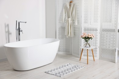 Stylish bathroom interior with ceramic tub and beautiful bouquet of roses on coffee table