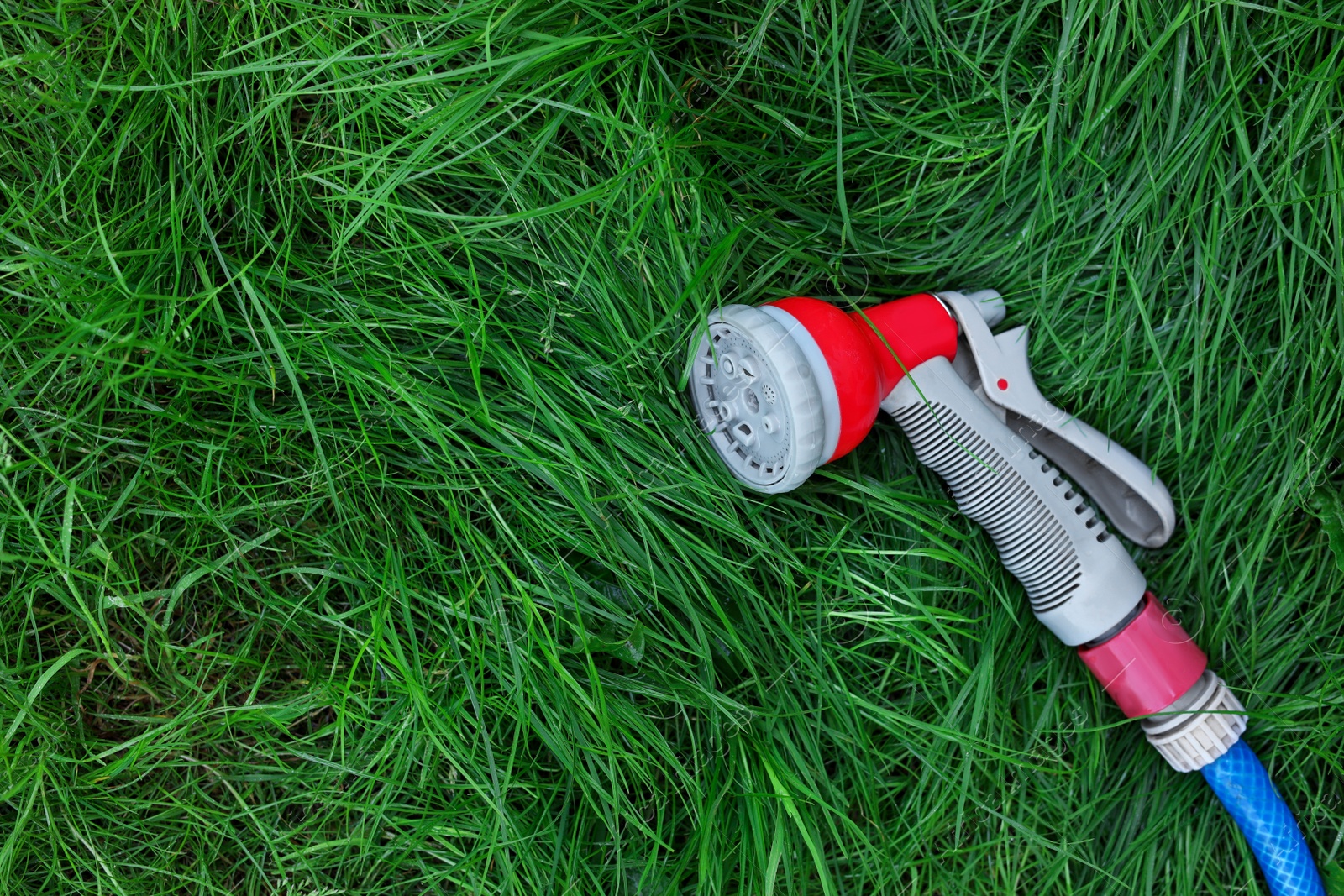 Photo of Watering hose with sprinkler on green grass outdoors, top view. Space for text