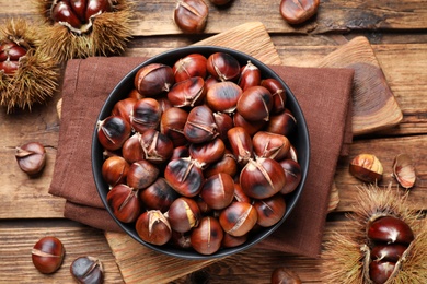 Photo of Delicious roasted edible chestnuts on wooden table, flat lay