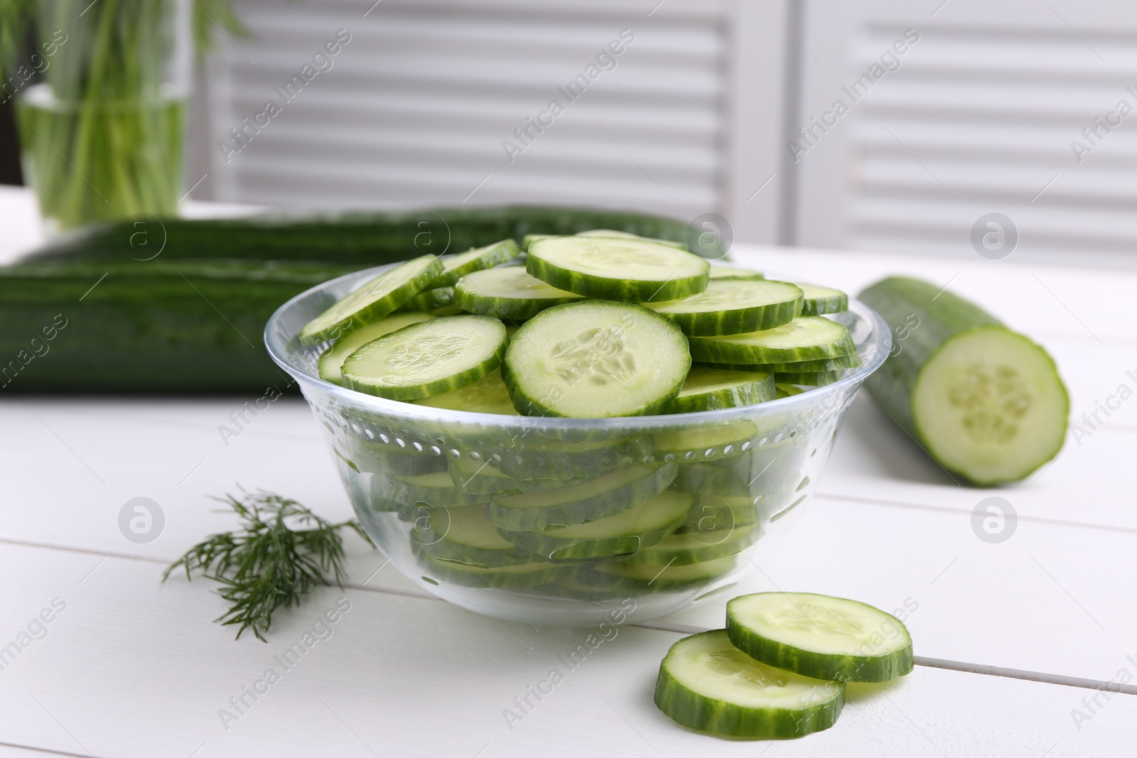 Photo of Cut cucumber in glass bowl, fresh vegetables and dill on white wooden table, closeup