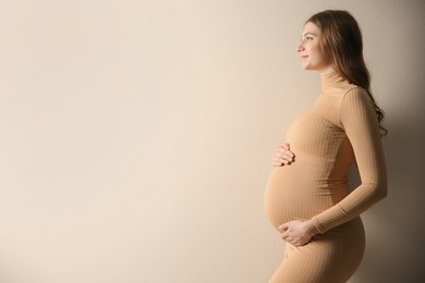 Happy pregnant woman touching her belly on beige background. Space for text