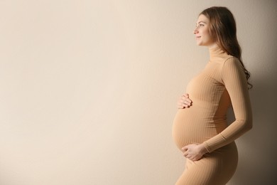 Photo of Happy pregnant woman touching her belly on beige background. Space for text