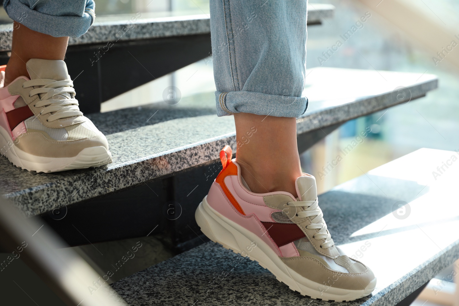 Photo of Young woman wearing stylish sneakers on grey stairs indoors, closeup