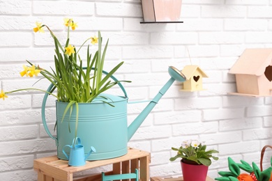 Photo of Beautiful daffodils in watering can on wooden crate near white brick wall indoors