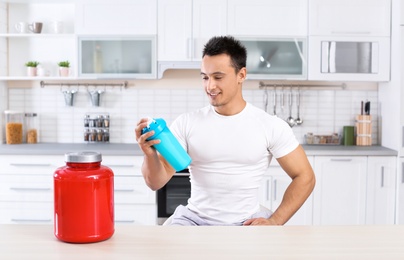 Photo of Man with protein shake in bottle and jar of powder in kitchen