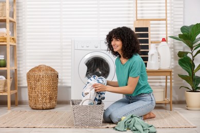 Photo of Happy woman with laundry near washing machine indoors