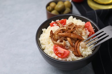 Tasty couscous with mushrooms and tomatoes on grey table, closeup. Space for text