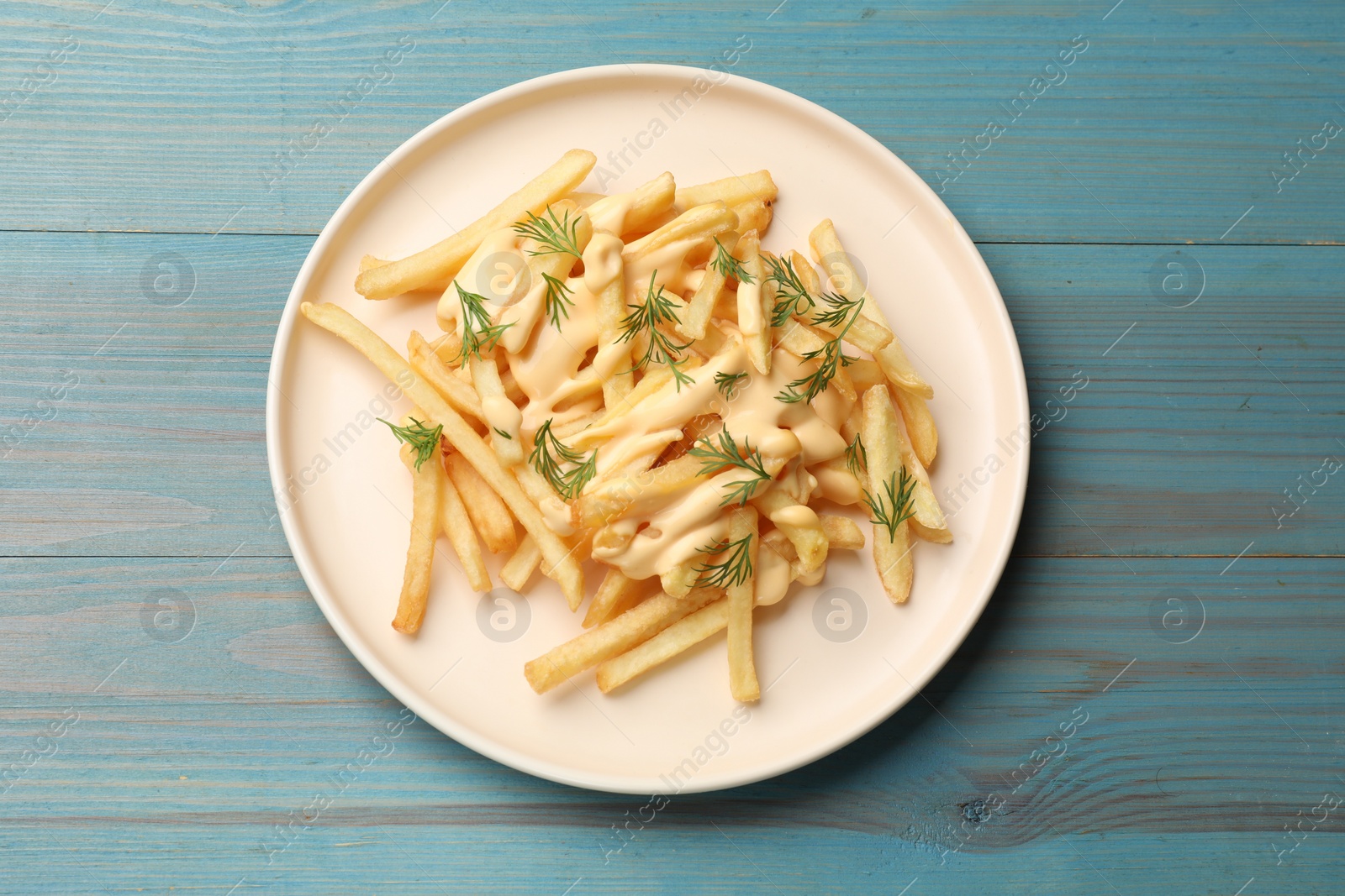 Photo of Delicious french fries with cheese sauce and dill on light blue wooden table, top view