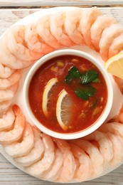 Photo of Tasty boiled shrimps with cocktail sauce and lemon on white wooden table, top view