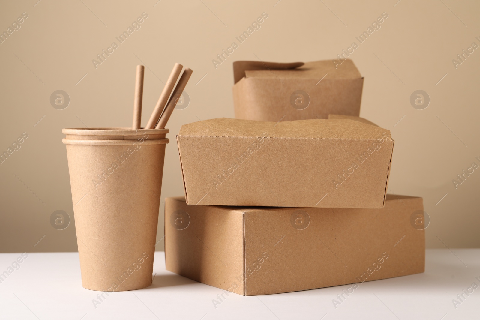 Photo of Eco friendly food packaging. Paper containers and straws on white table against beige background