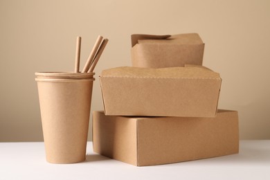 Photo of Eco friendly food packaging. Paper containers and straws on white table against beige background