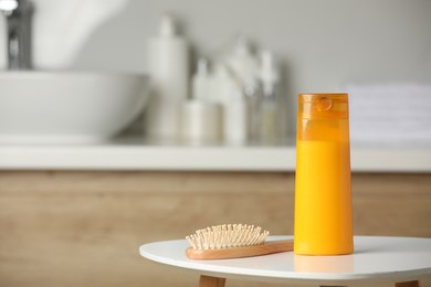 Bottle of shampoo and wooden hairbrush on white table in bathroom, space for text